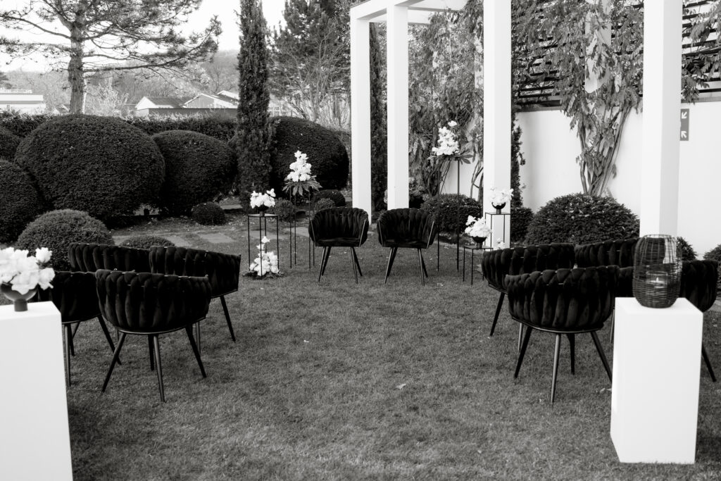 Schwarze Stühle in einem Garten für eine Veranstaltung im Freien in Brandenburg, mit Blumen und Grünzeug drum herum - perfekt für eine Zeremonie, die von einer Freien Traurednerin in der Nähe von Berlin geleitet wurde.